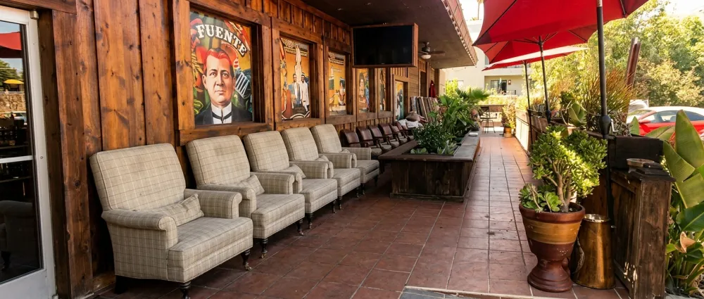 Outdoor patio lounge with plaid armchairs, red umbrellas and vintage Fuente posters